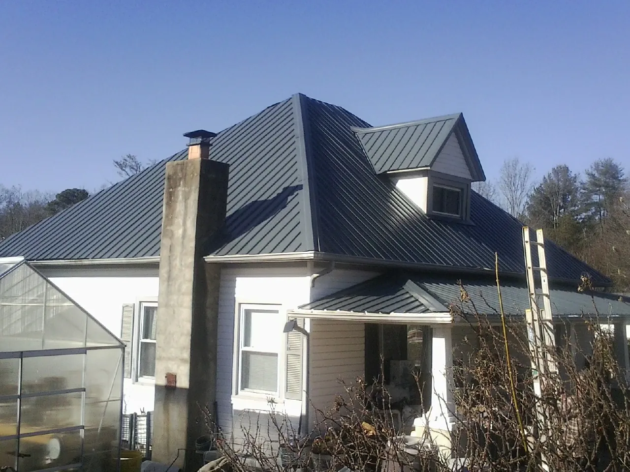 Dark blue standing seam metal roof on a white farmhouse with dormer — Slate & Tile Roof Repair by Roofing Brothers in Cold Spring Harbor