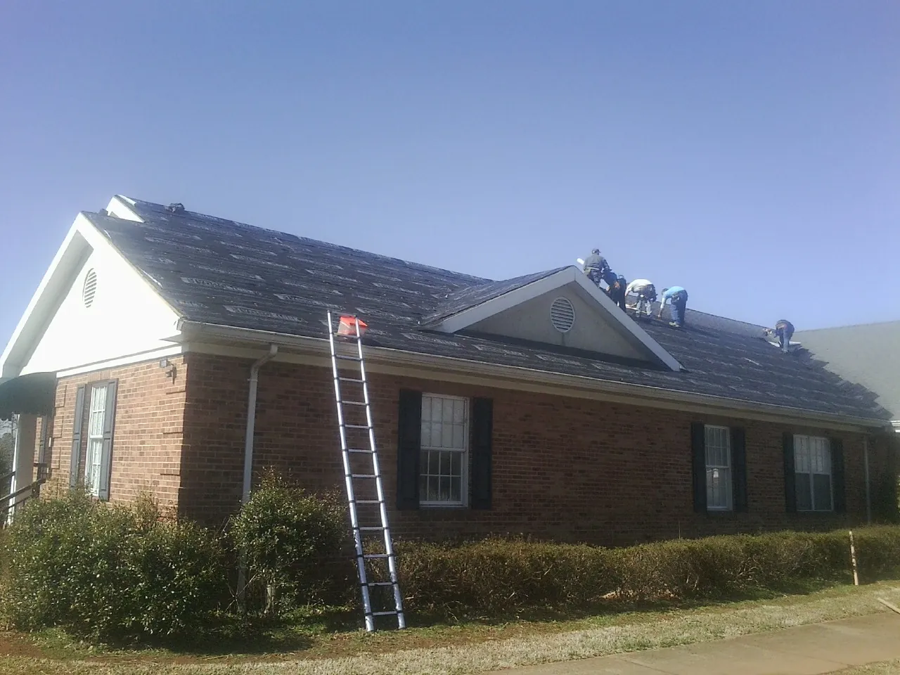 Crew tearing shingles off a brick ranch roof with a ladder set — Metal Roof Repair work by our crew in Cold Spring Harbor