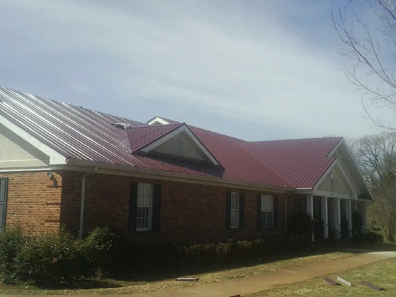 Red metal roof with gabled entries on a long brick building, from a Hail Damage Roof Repair job in Cold Spring Harbor