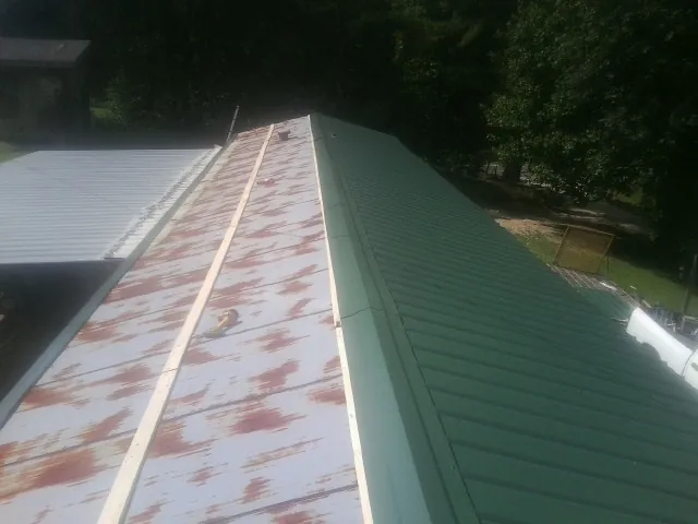 Old rusted panels beside newly installed green metal roofing — Wind Damage Roof Repair by Roofing Brothers in Cold Spring Harbor