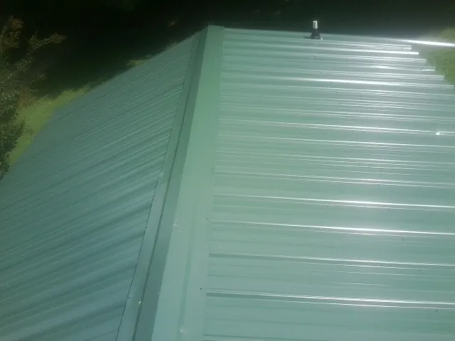 New green metal panels meeting at the ridge of a roof — Flat Roof Repair work by our crew in Cold Spring Harbor