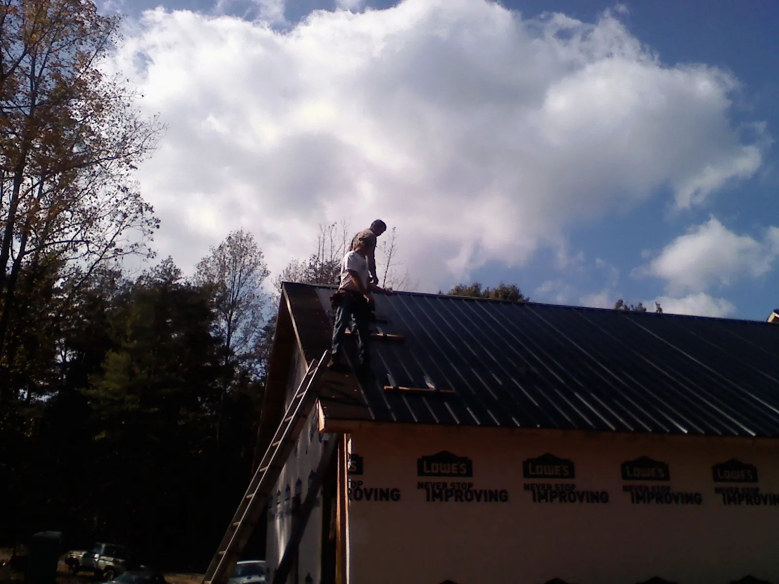Roofer fastening dark metal panels high against a cloudy sky, from a Roof Inspection job in Cold Spring Harbor