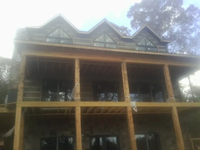 Dormers and porch framing on a large log home under construction — Roof Coating work by our crew in Cold Spring Harbor