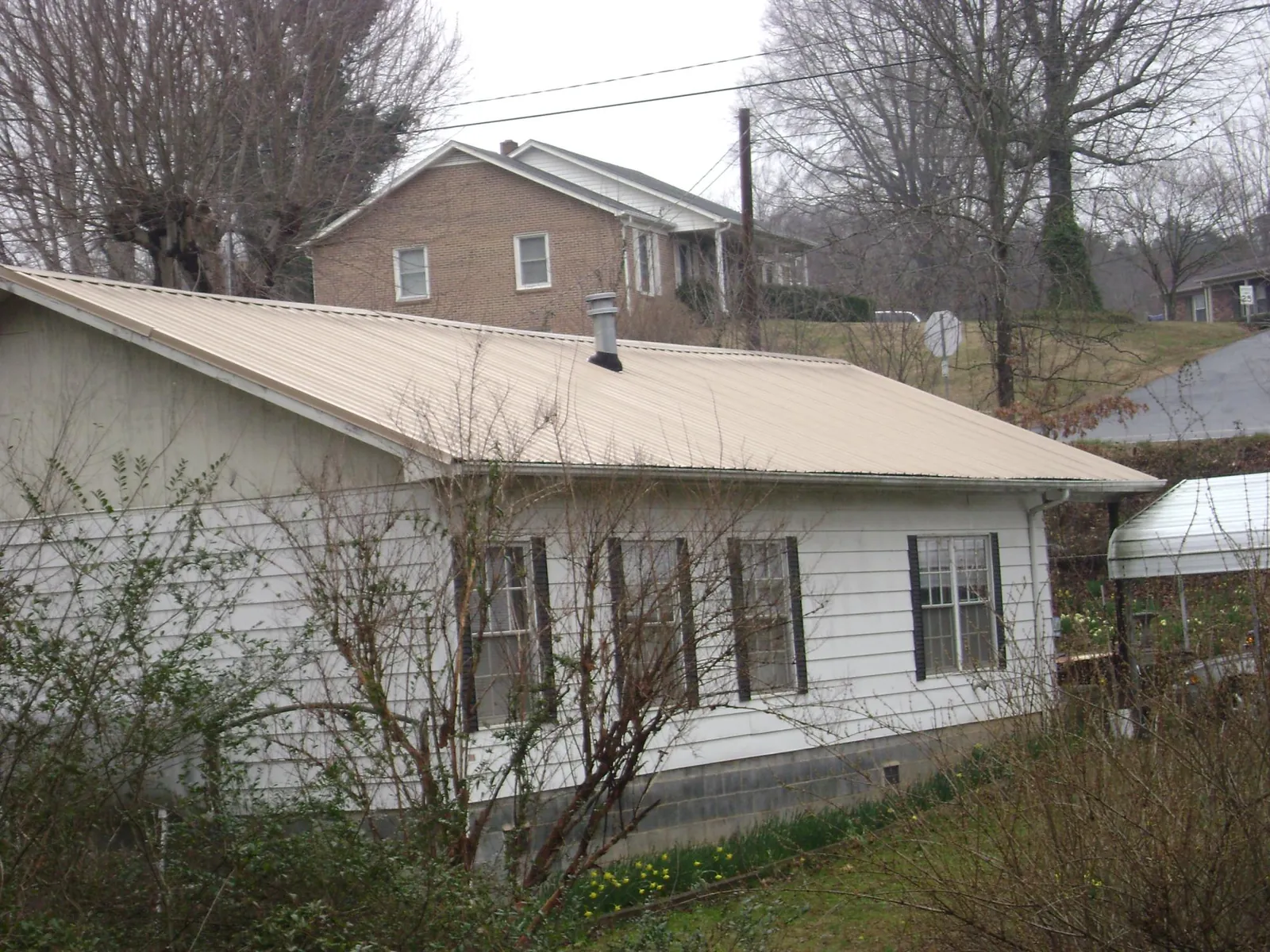 Tan metal roof on a white sided house set into a hillside — Commercial Roofing by Roofing Brothers in Cold Spring Harbor
